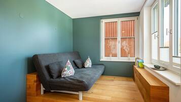 A room with a grey sofa, wooden bench, and a window with blinds.