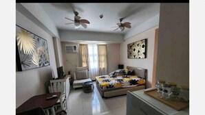 A bedroom with a bed, a desk, a chair, a ceiling fan, and artwork on the walls. - 101 Newport Blvd (Pasay)