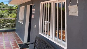 A building with a grey exterior, a covered outdoor area with a bench, and a window with white bars.
