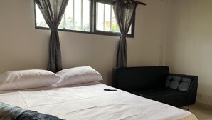 A room with a bed, a black chair, and a window with curtains.