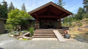 A wooden cabin with a covered porch, gravel driveway, and surrounding greenery. - Family adventures await in this ocean front house!  (Pet friendly!)
 (Quathiaski Cove)