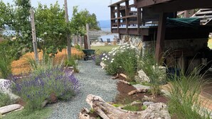 A garden with a gravel path, various plants, a wooden structure, and a view of the water. - Family adventures await in this ocean front house!  (Pet friendly!)
 (Quathiaski Cove)