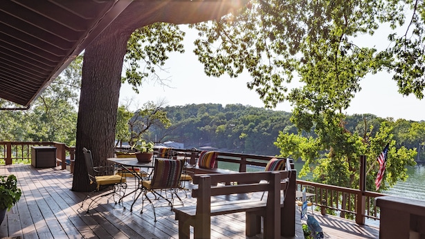 A wooden deck with outdoor furniture, a table, and chairs, overlooking a lake and forested hills. - Waterfront lake house with your own private dock and amazing views.  (Eucha)