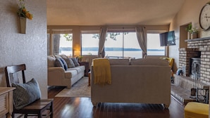 A living room with a sofa, a chair, a fireplace, and a large window overlooking a body of water. - Waterfront lake house with your own private dock and amazing views.  (Eucha)