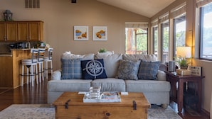A cozy living room with a sofa, coffee table, and a dining area with chairs and a kitchen in the background. - Waterfront lake house with your own private dock and amazing views.  (Eucha)