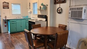 Un coin repas avec une table et des chaises en bois, une cuisine en arrière-plan et un panneau indiquant « LAC ».