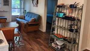 Un salon chaleureux avec un canapé bleu, une table à manger en bois et une étagère en métal contenant des ustensiles de cuisine.