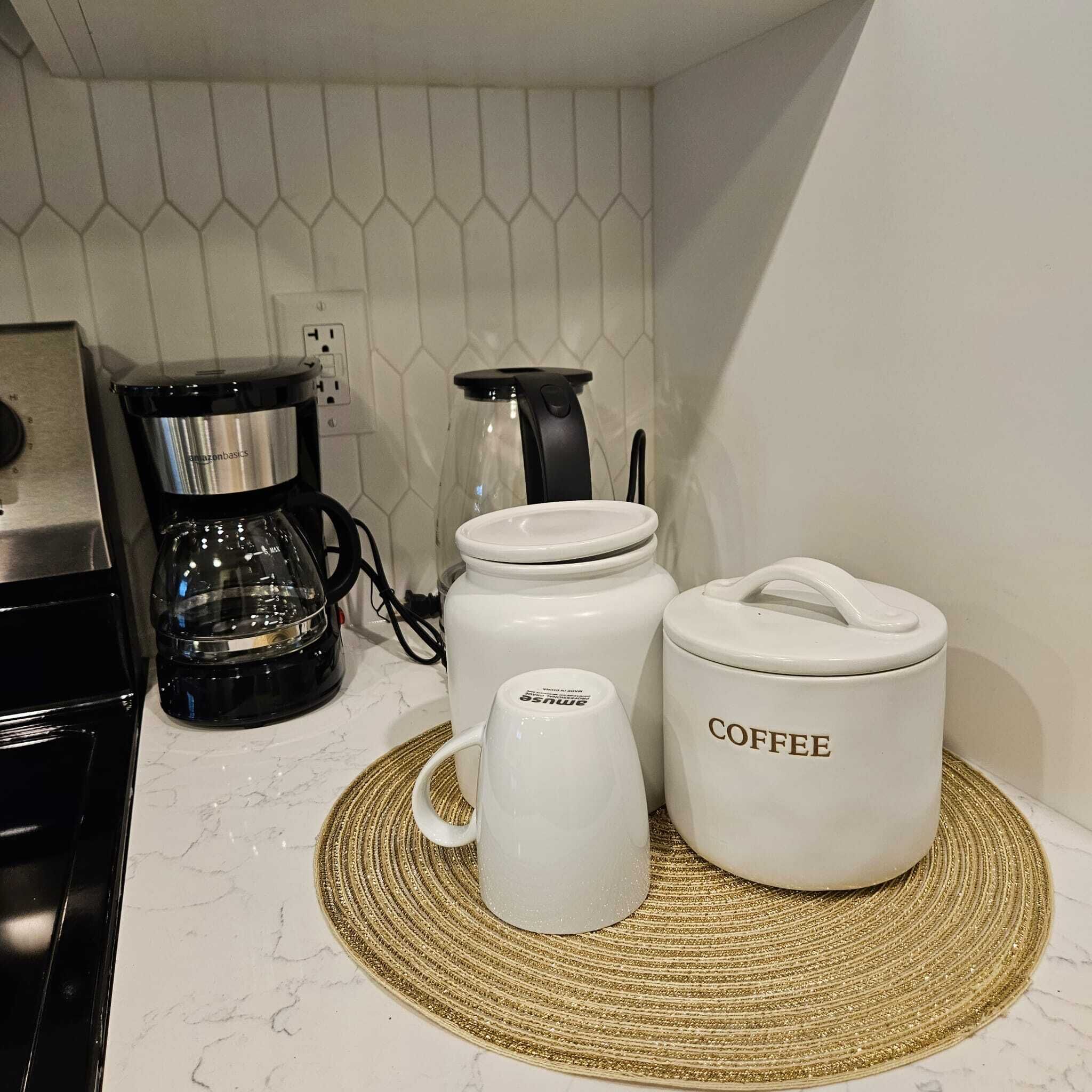 A kitchen with a coffee maker, a glass carafe, and two white containers labeled "COFFEE" on a marble countertop.