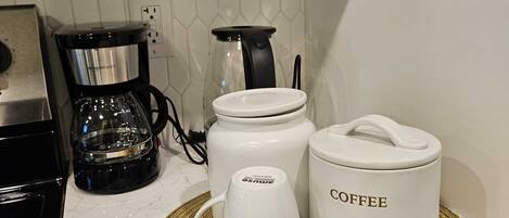 A kitchen with a coffee maker, a glass carafe, and two white containers labeled "COFFEE" on a marble countertop.