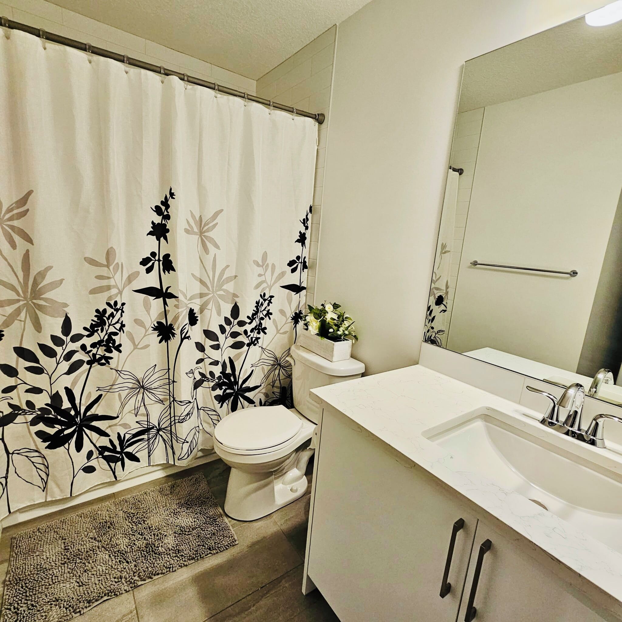 A bathroom with a toilet, sink, mirror, and shower curtain with a floral pattern.