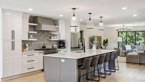 A modern kitchen with white cabinetry, a central island with bar stools, and pendant lighting.