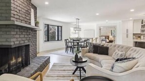 A modern living room with a fireplace, a dining area, and a kitchen.