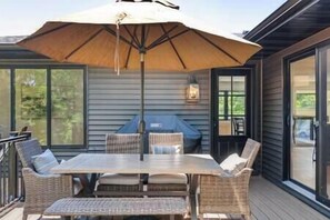 En täckt uteplats med ett bord och stolar, en grill och ett stort parasoll.