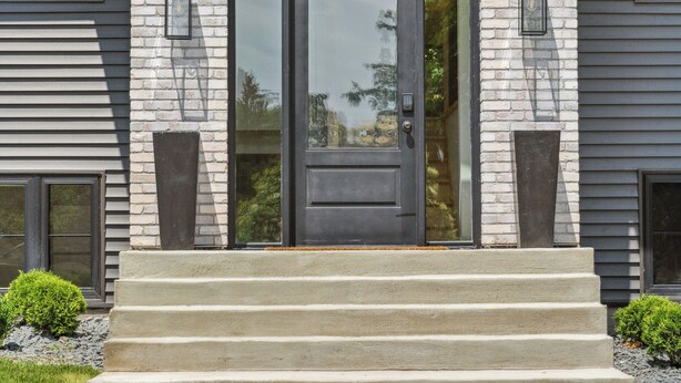 A modern two-story house with a prominent front entrance, a stone facade, and a wooden beam roof.