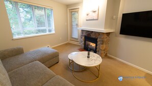 A living room with a stone fireplace, a flat-screen TV, and a beige sectional sofa.