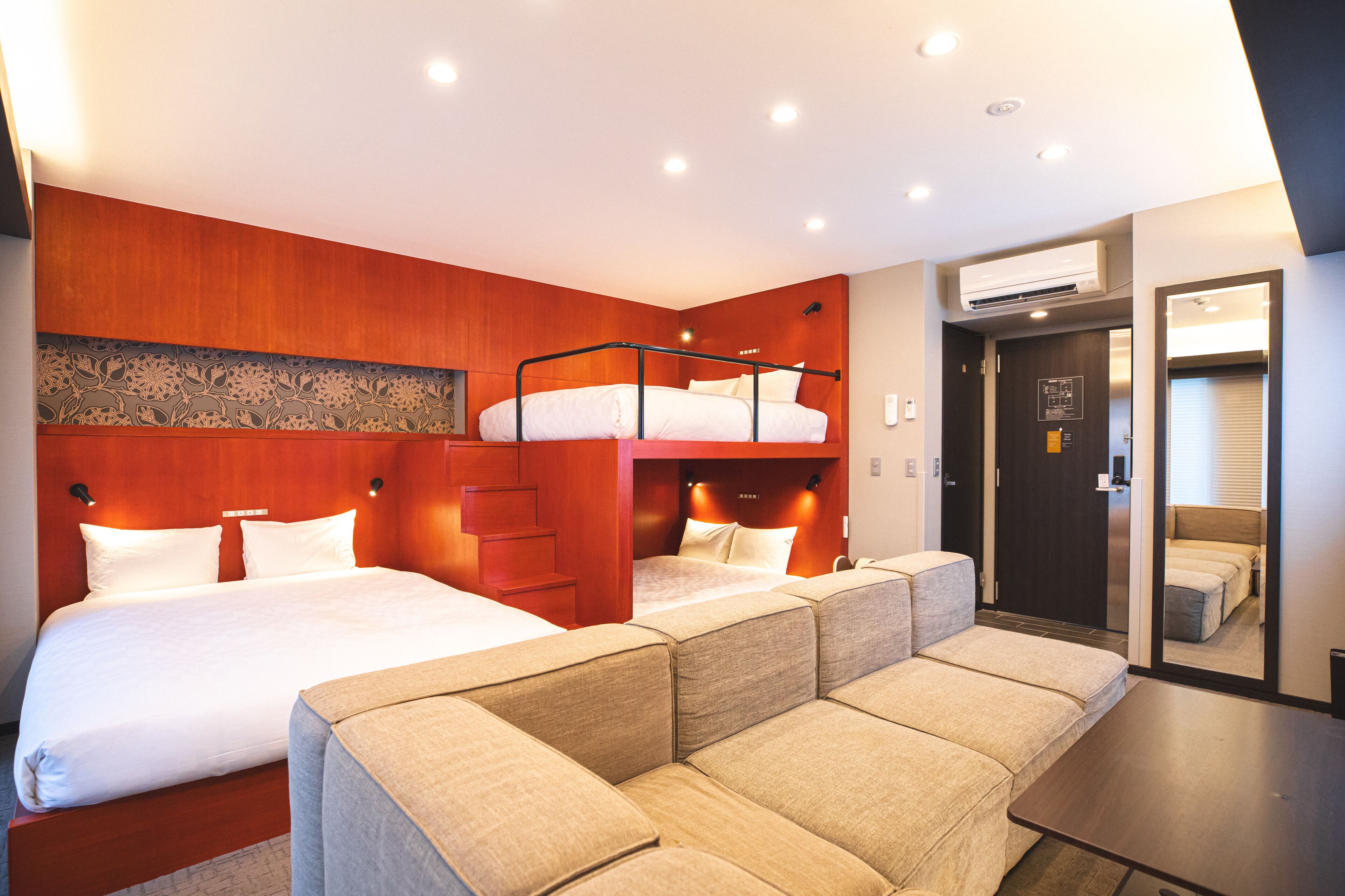 A modern hotel room with a bunk bed, a sofa, and a desk.