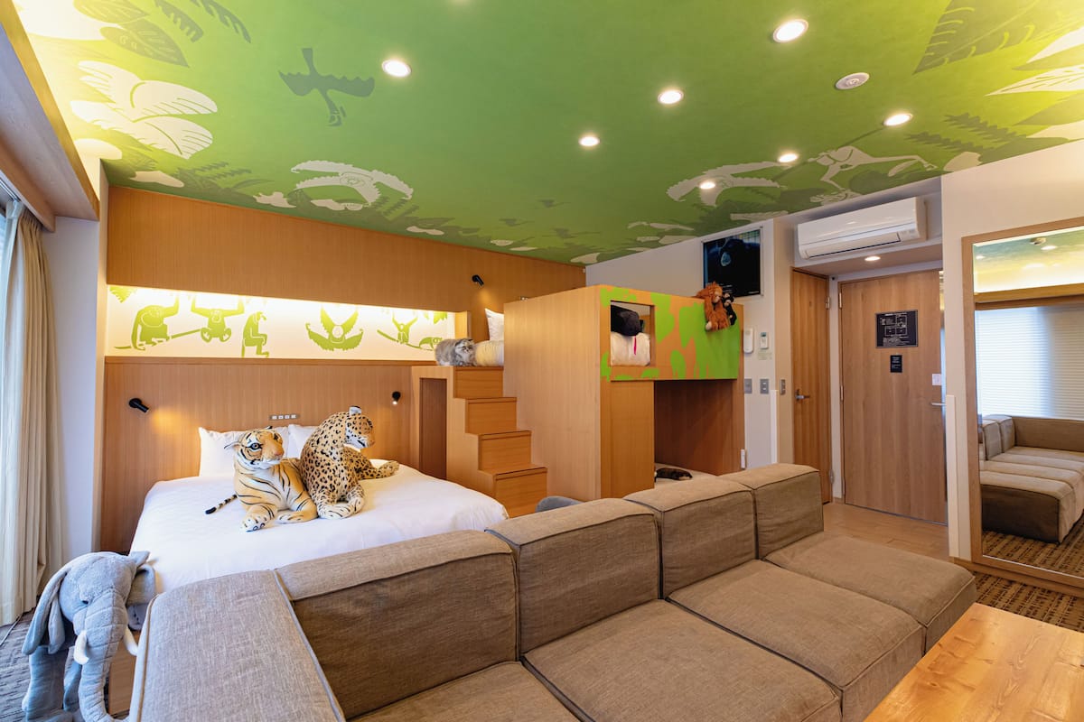 A hotel room with a bed, a sofa, a staircase, and a green ceiling with leaf patterns.