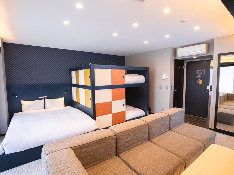 A modern hotel room with a large bed, a bunk bed, and a sofa area.