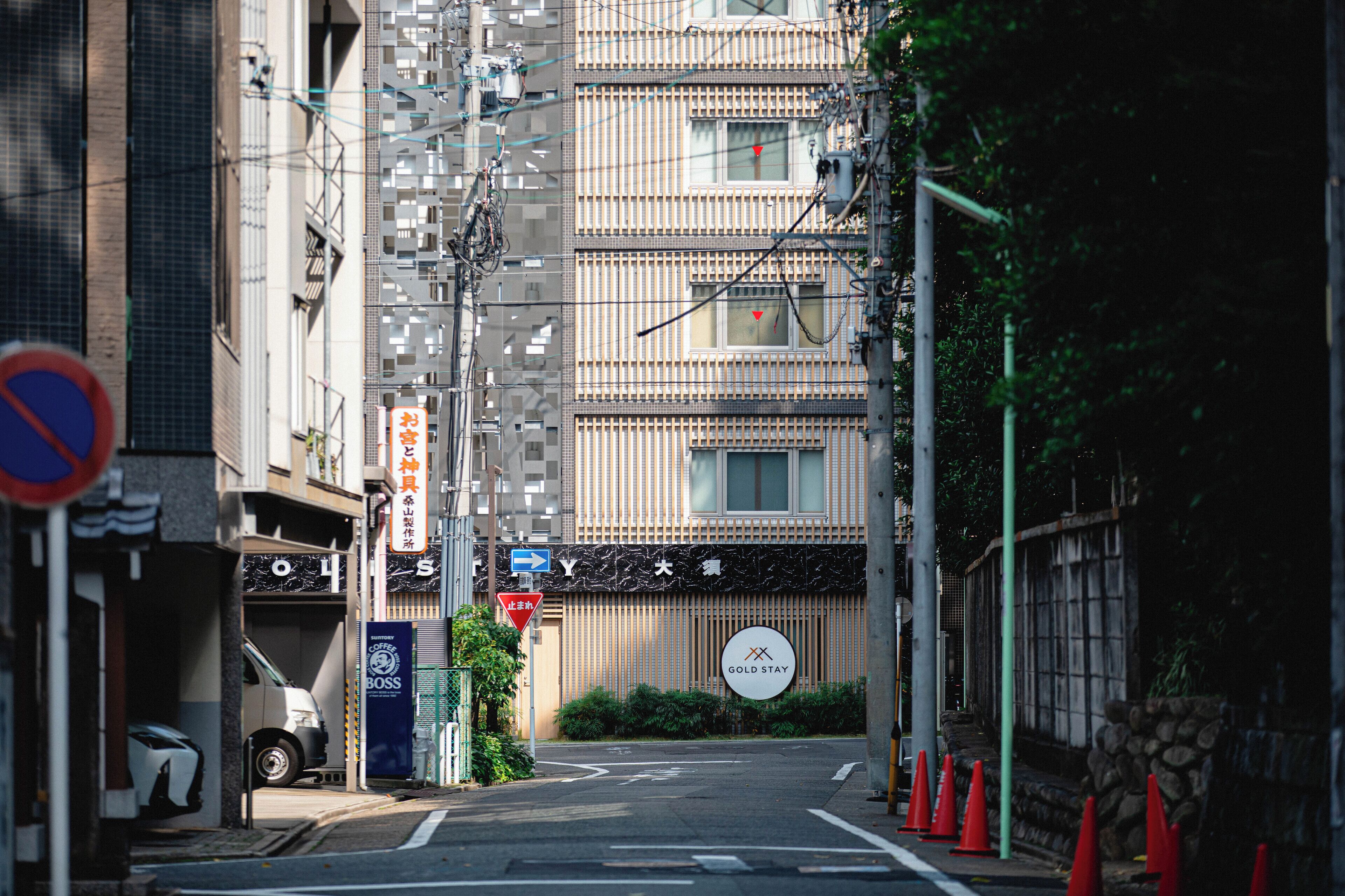 A narrow urban street with a building featuring a sign for "Gold Stay."