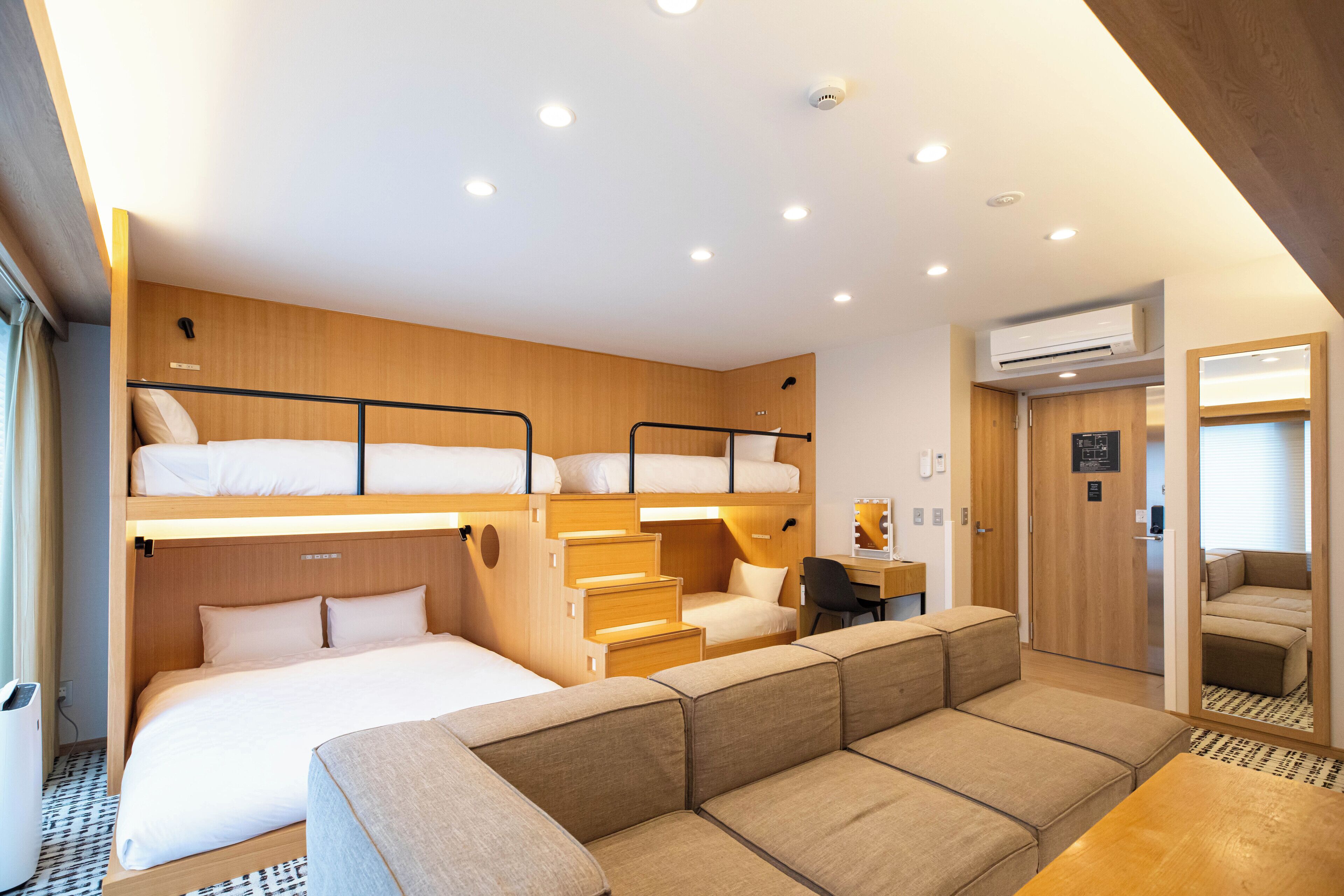 A compact hotel room with bunk beds, a sofa, a desk, and a small kitchenette.