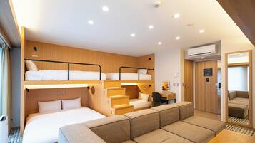 A compact hotel room with bunk beds, a sofa, a desk, and a small kitchenette.