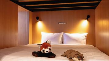 Habitación de hotel con cama, dos almohadas, una lámpara de pared y un peluche.