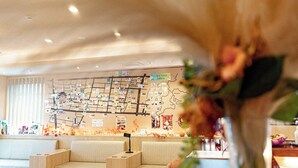 Un hall d’hôtel avec un mur décoré de photos et de notes, des coins salon et un grand vase rempli de fleurs.