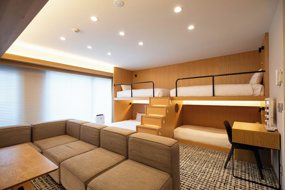 A compact, modern room with bunk beds, a sofa, a desk, and a patterned rug.