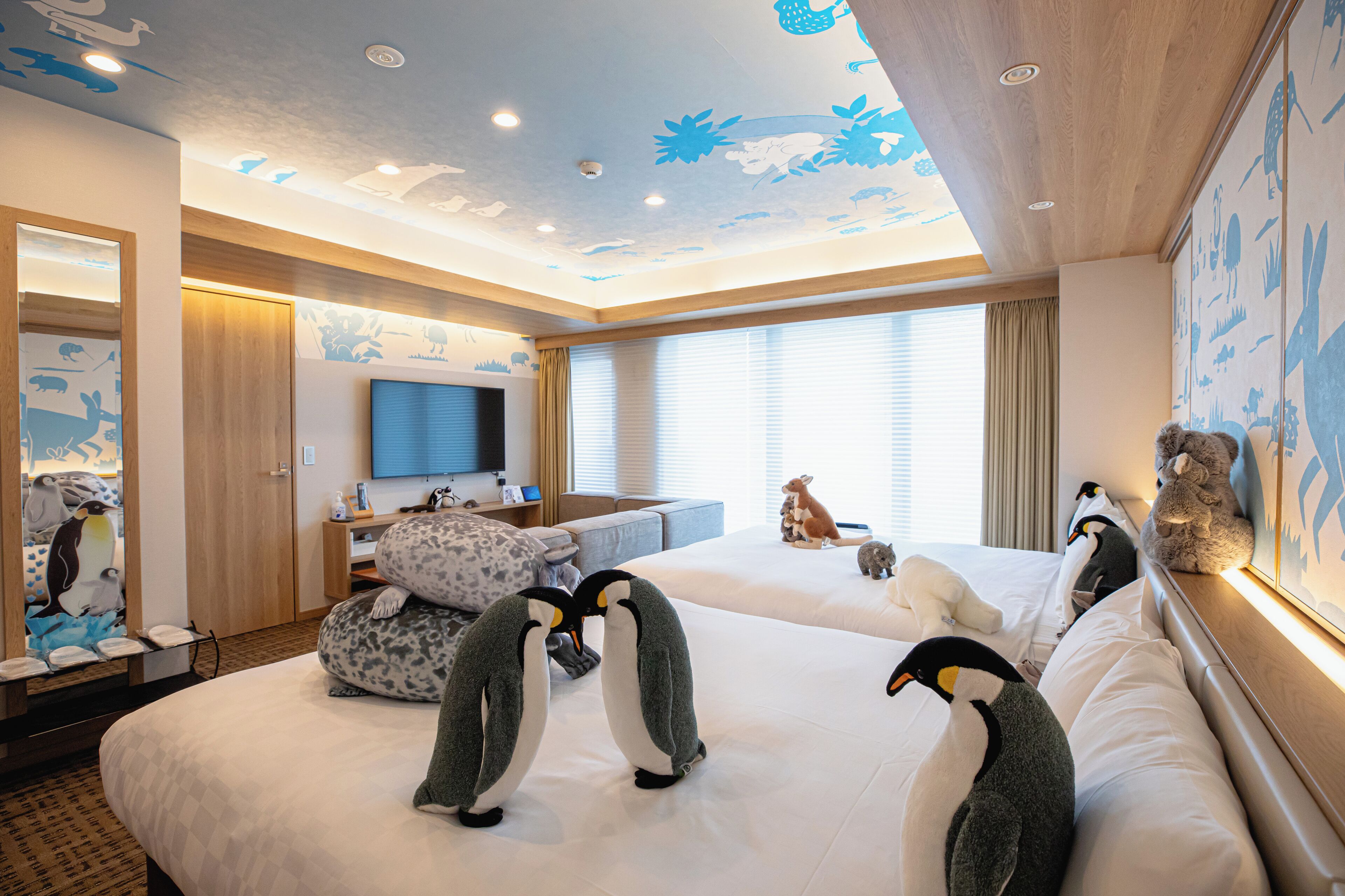 A hotel room with two beds, a TV, a desk, and penguin-themed decor.