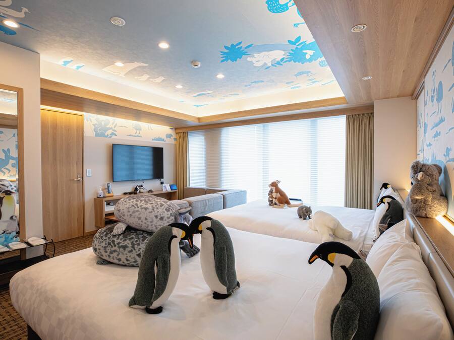 A hotel room with two beds, a TV, a desk, and penguin-themed decor.