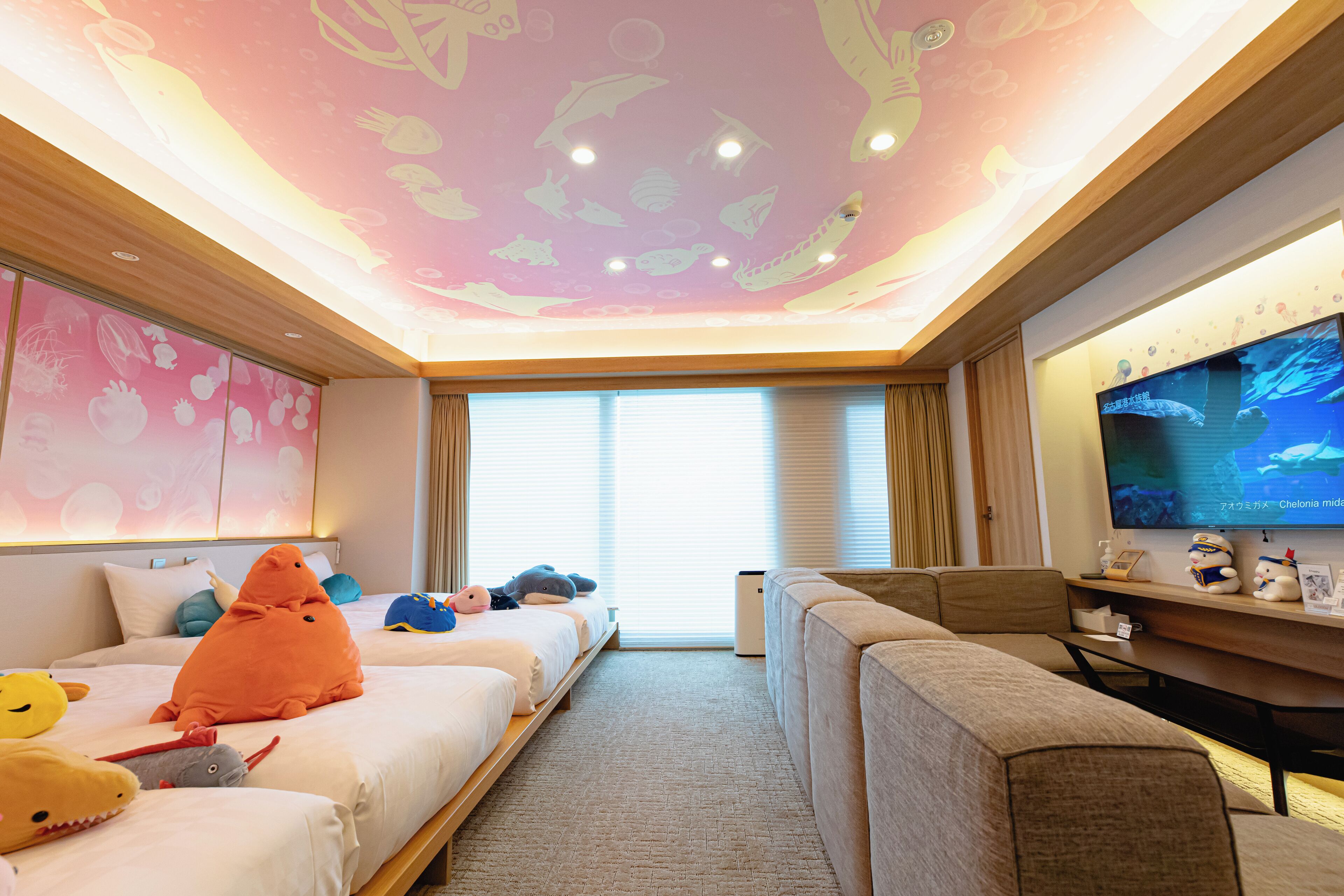 Una habitación de hotel con cama, sofá, televisor y techo decorado con motivos marinos.