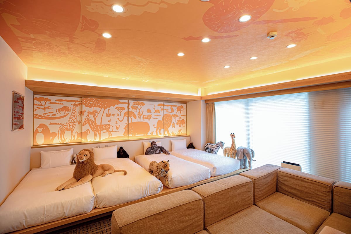A hotel room with two beds, a large mural of animals on the wall, and a window with blinds.