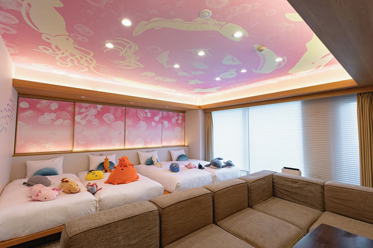A hotel room with two beds, a sofa, and a ceiling with a marine-themed mural.
