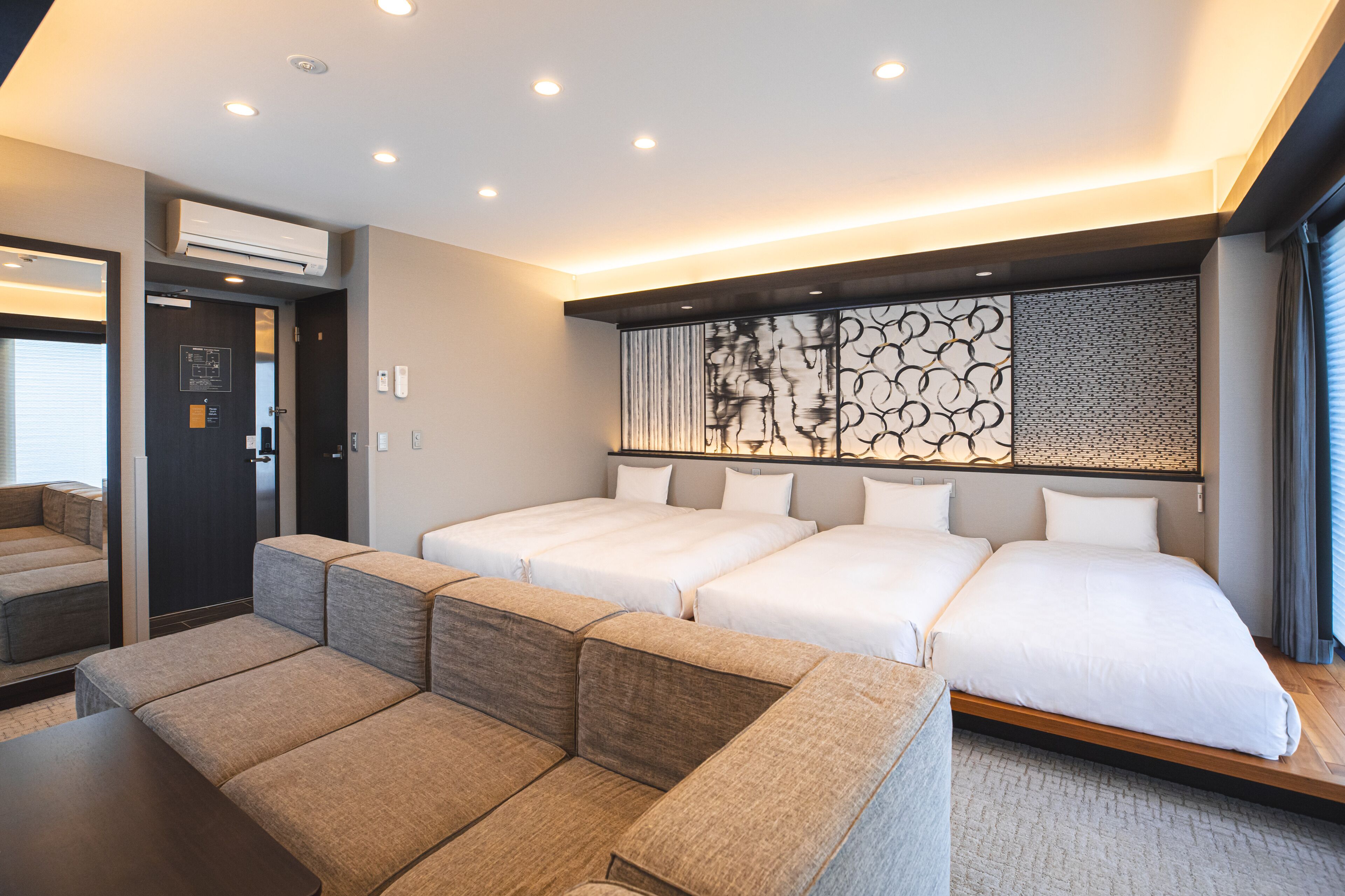 Een moderne hotelkamer met een bank, twee bedden, een decoratieve muur en een groot raam.