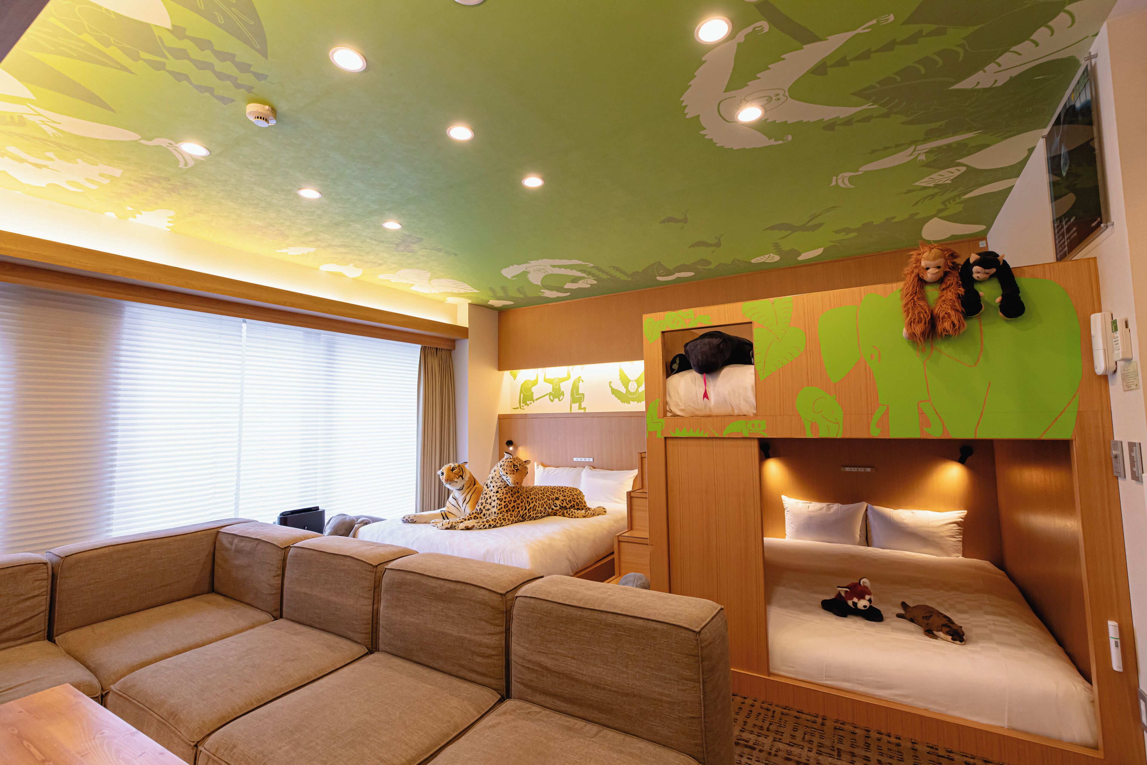 A hotel room with a green ceiling, two beds, a sofa, and a wall-mounted TV.