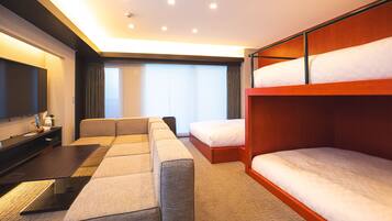 A hotel room with a sofa, a bed, a TV, and a window with blinds.