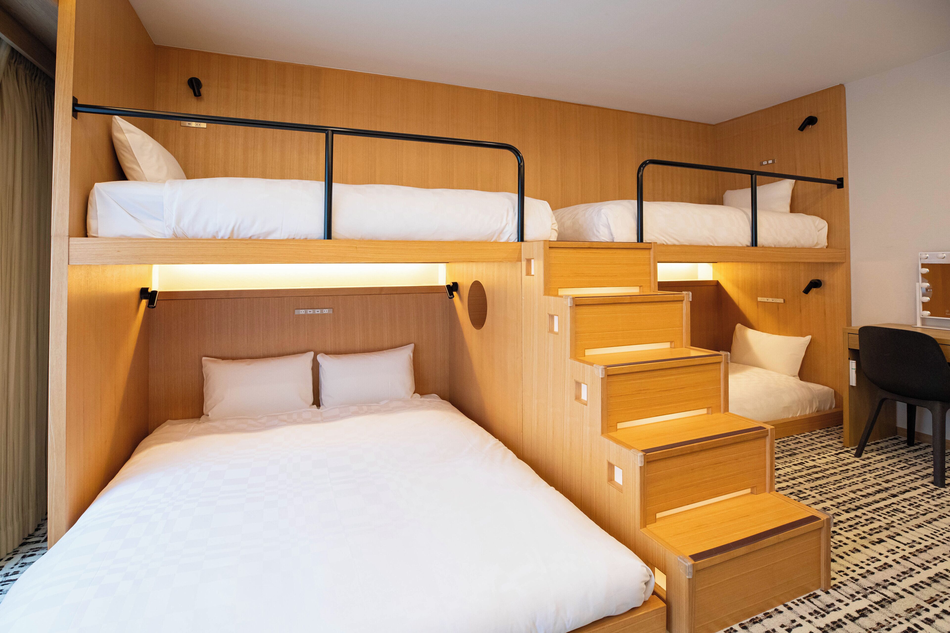 A bunk bed room with a desk and chair, wooden walls, and a patterned floor.