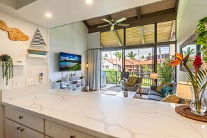Une cuisine moderne dotée d’un plan de travail en marbre, d’un ventilateur de plafond et d’une grande fenêtre donnant sur un balcon aménagé avec du mobilier d’extérieur.