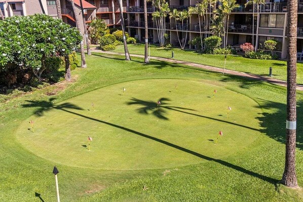 A golf course with a well-maintained lawn, several holes marked with flags, and a building with balconies in the background.