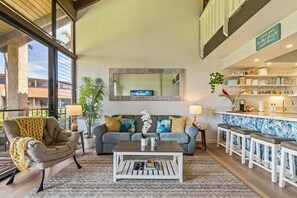Un salon comprenant un canapé, un fauteuil, une table basse et un coin bar avec des tabourets.