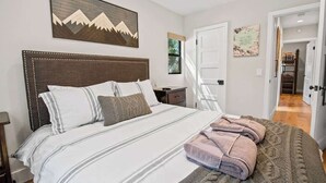 Ein Schlafzimmer mit einem großen Bett, einem Kopfteil, einem Nachttisch und einem an der Wand hängenden Gemälde.