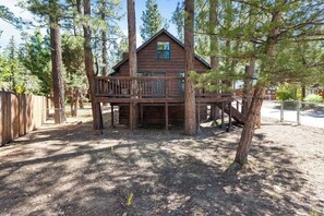 Une cabane en bois dotée d’une terrasse, entourée de grands arbres.