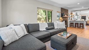 Ein modernes Wohnzimmer mit einem Ecksofa, einem Couchtisch und einer sichtbaren Küchenzeile im Hintergrund.