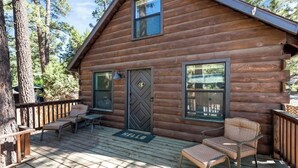 Eine Blockhütte mit einer Terrasse, zwei Fenstern und einer Tür mit Rautenmuster.