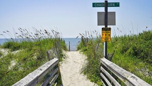A beach path with a wooden fence, a street sign for Chadburn St, and a social distancing sign.