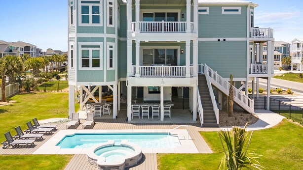 A multi-level waterfront property with a pool, outdoor seating, and a hot tub.