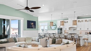 A spacious living area with a large L-shaped sofa, a dining table, and a kitchen area with white cabinets and a herringbone backsplash.
