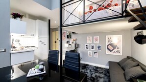 Un apartamento moderno con cocina, comedor y sala de estar. Presenta un diseño estilo loft con escalera, sillas de cuero negro y sofá gris.