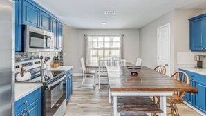 Una cocina con armarios azules, una mesa de comedor de madera y sillas blancas.