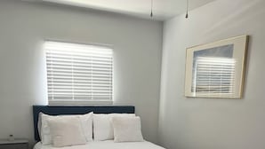 Une chambre à coucher avec un lit, des tables de chevet, un banc et une fenêtre avec des stores.
